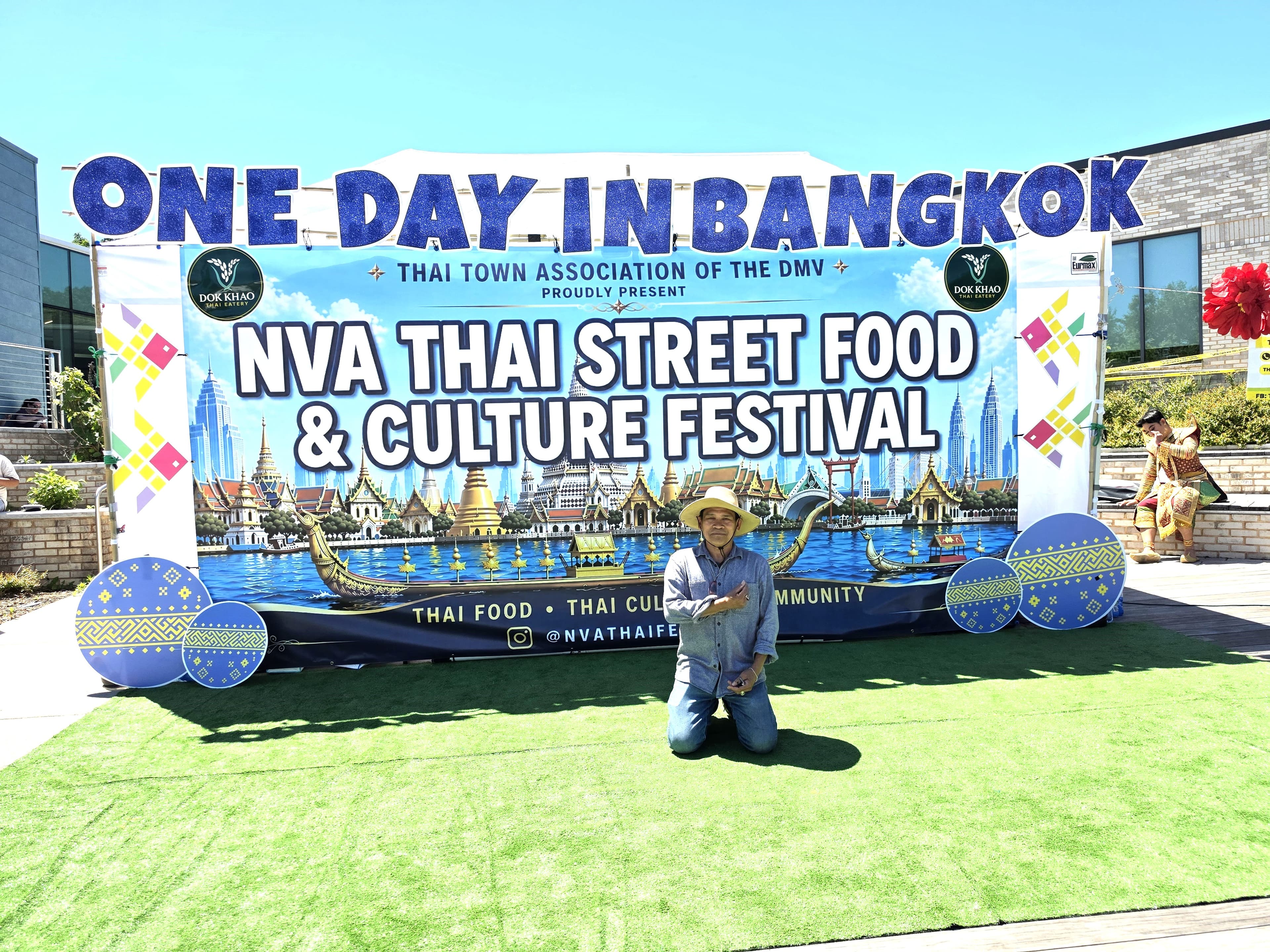 Man kneeling before a large NVA Thai Street Food and Culture Festival banner outdoors.