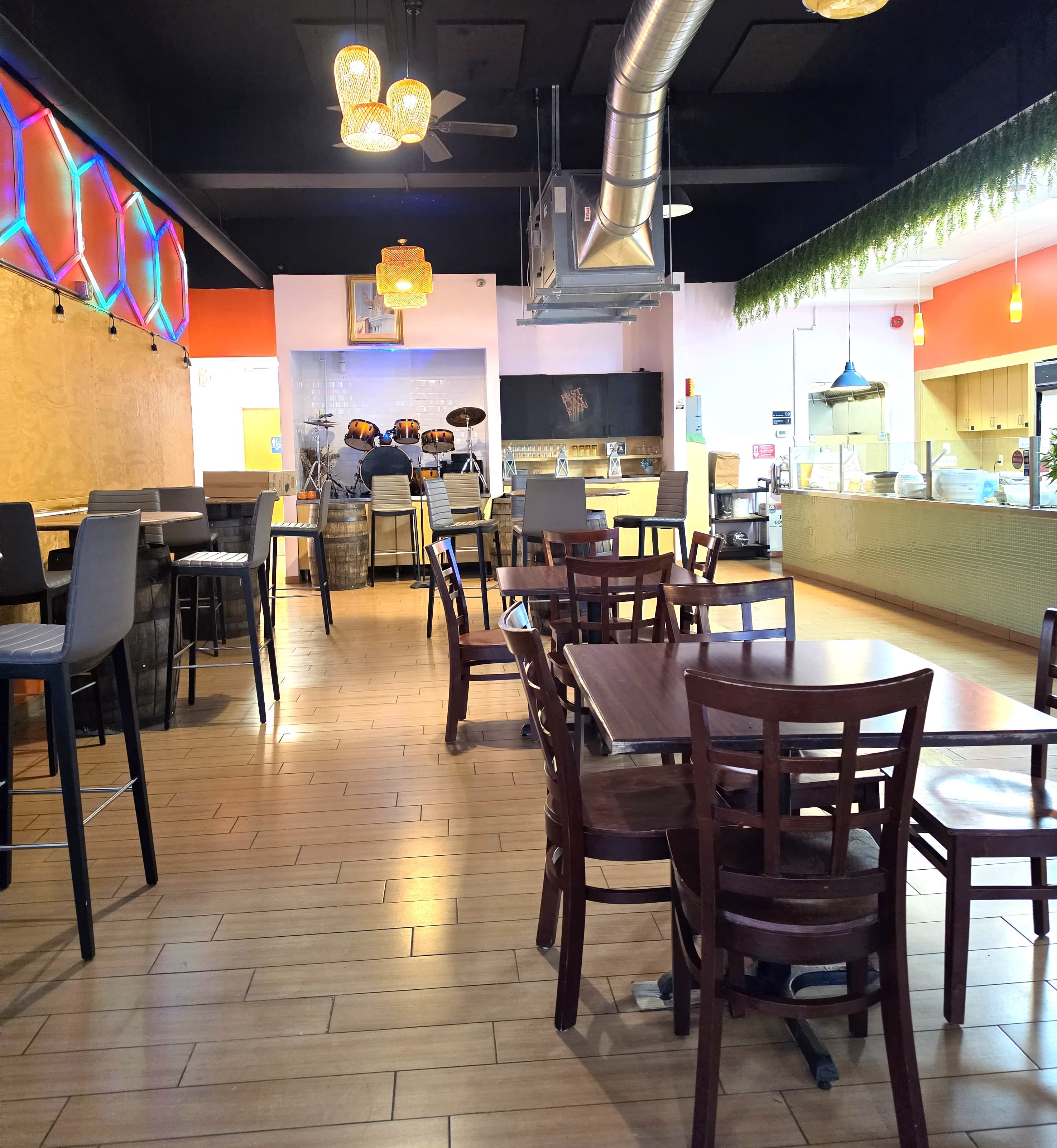 Vibrant restaurant interior with wooden tables, neon wall art, and a drum set.