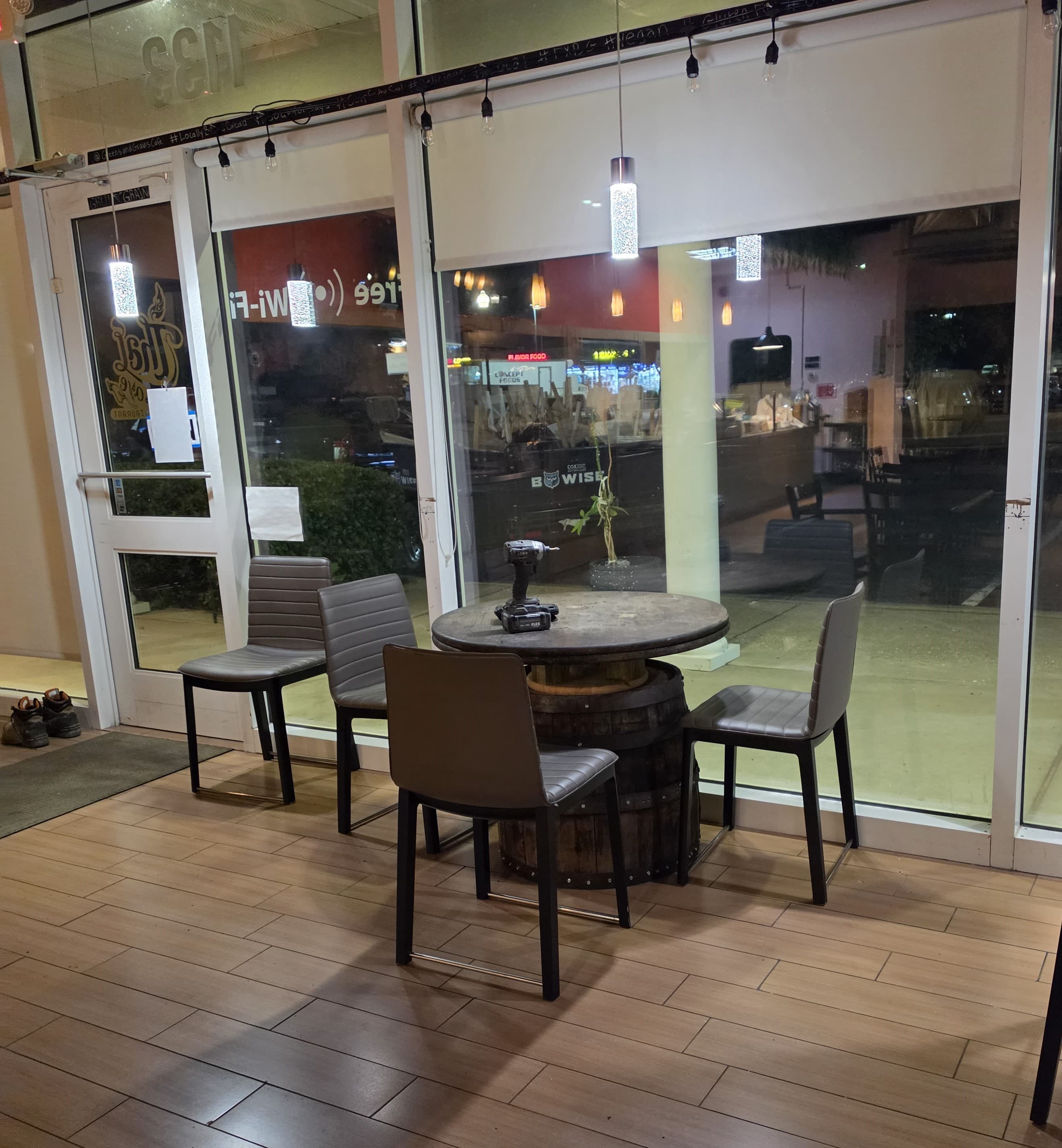 Grey chairs around a wooden barrel table with a power drill inside a restaurant.
