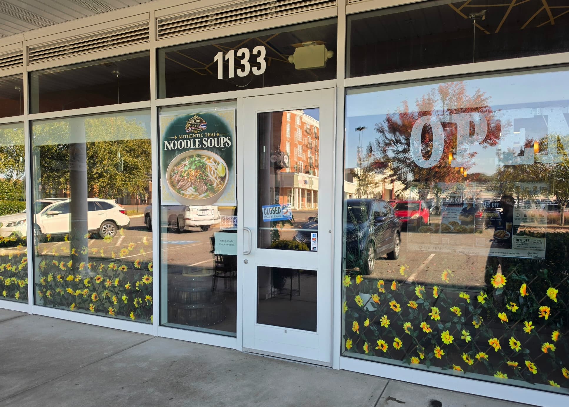 Storefront of Seri Thai restaurant with a noodle soup poster and sunflower window decals.