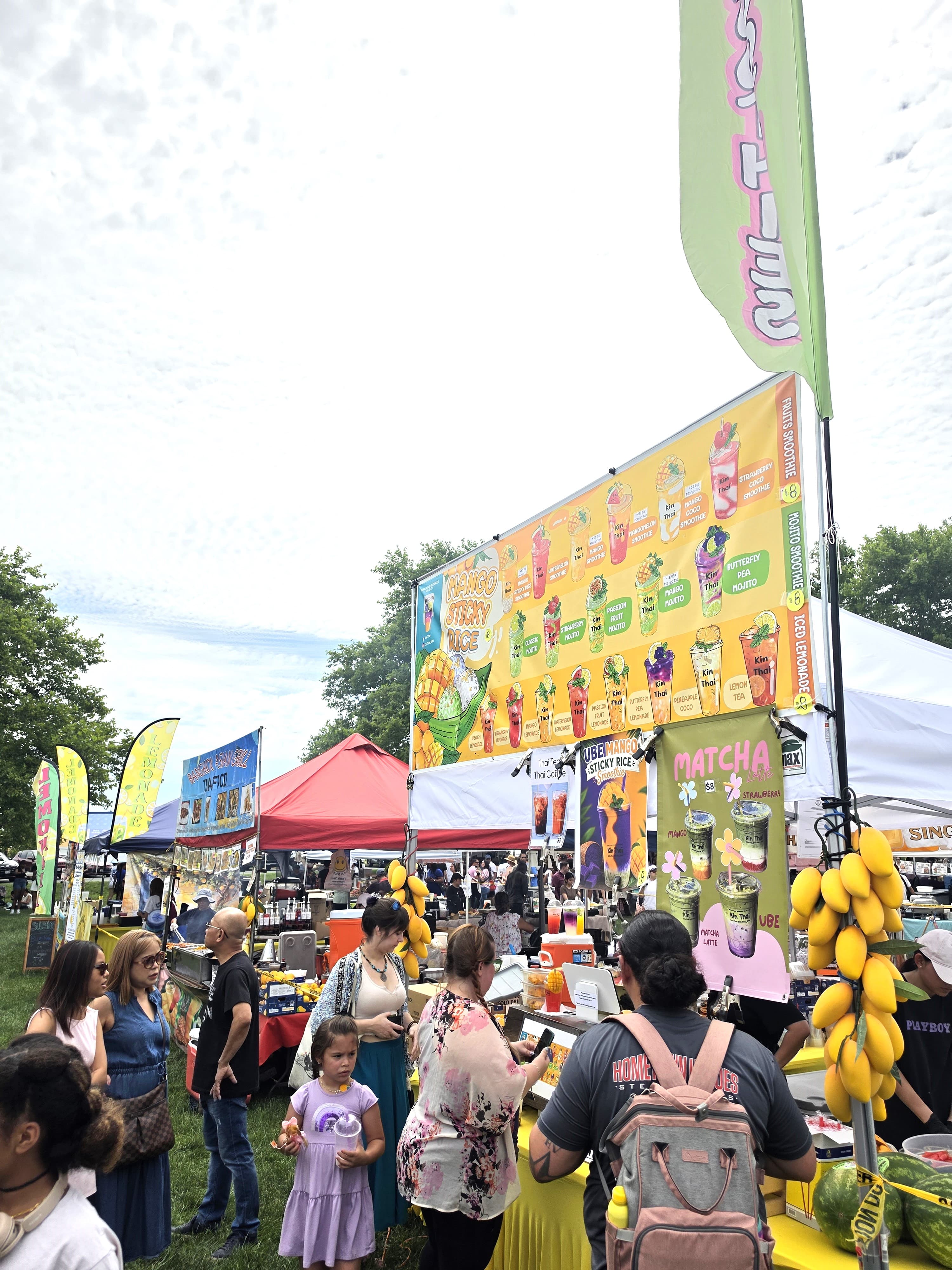 Vibrant outdoor food festival with people gathered around a colorful mango sticky rice stall.
