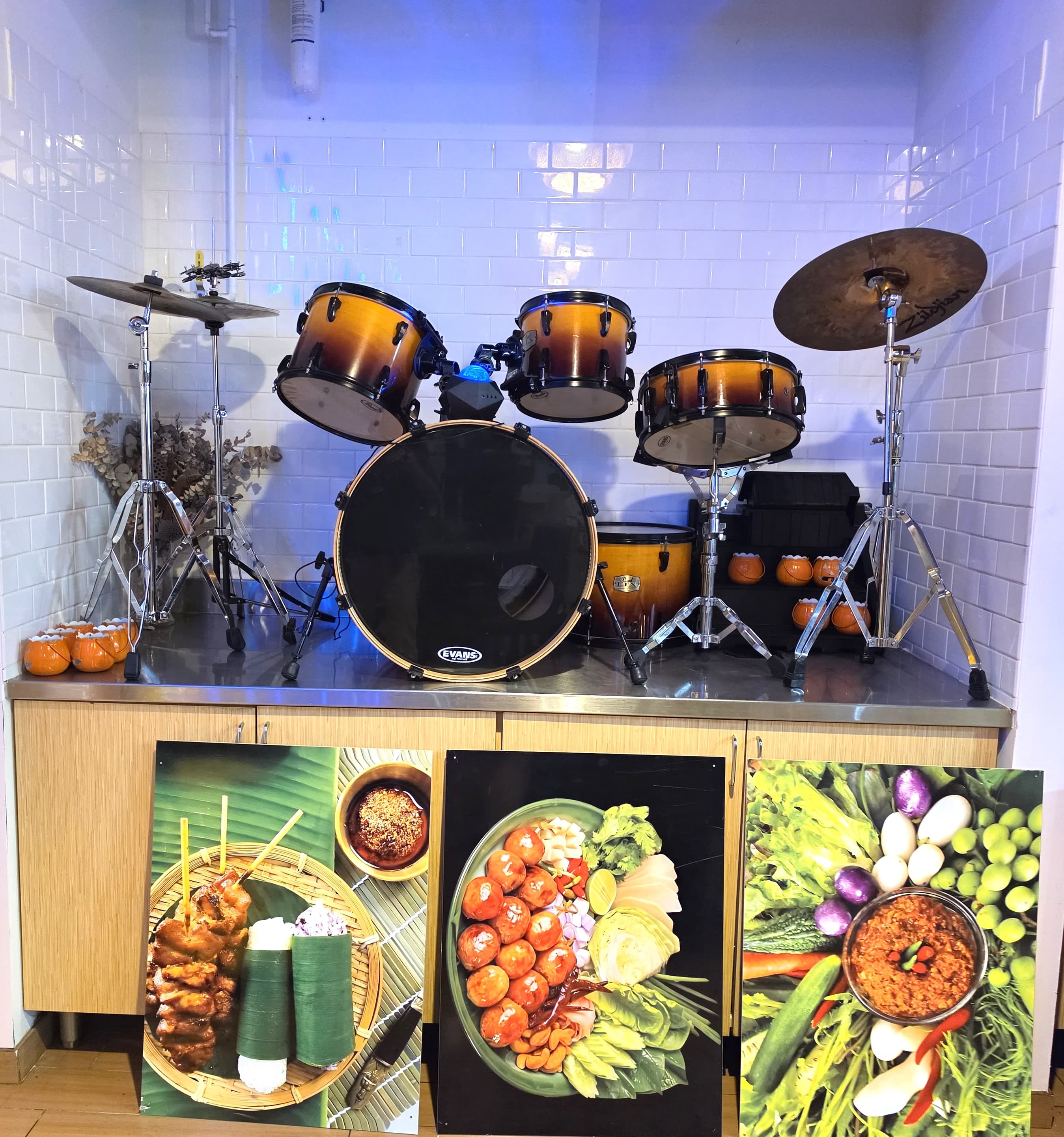 Sunburst drum set on a counter above three large posters of traditional Thai food.